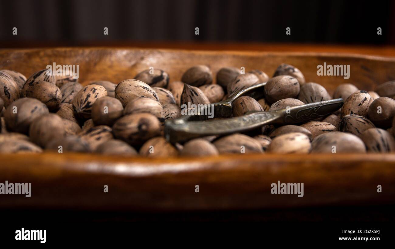 Raw in shell whole Pecan nuts in a wooden bowl on a wood table with a vintage nut cracker Stock Photo