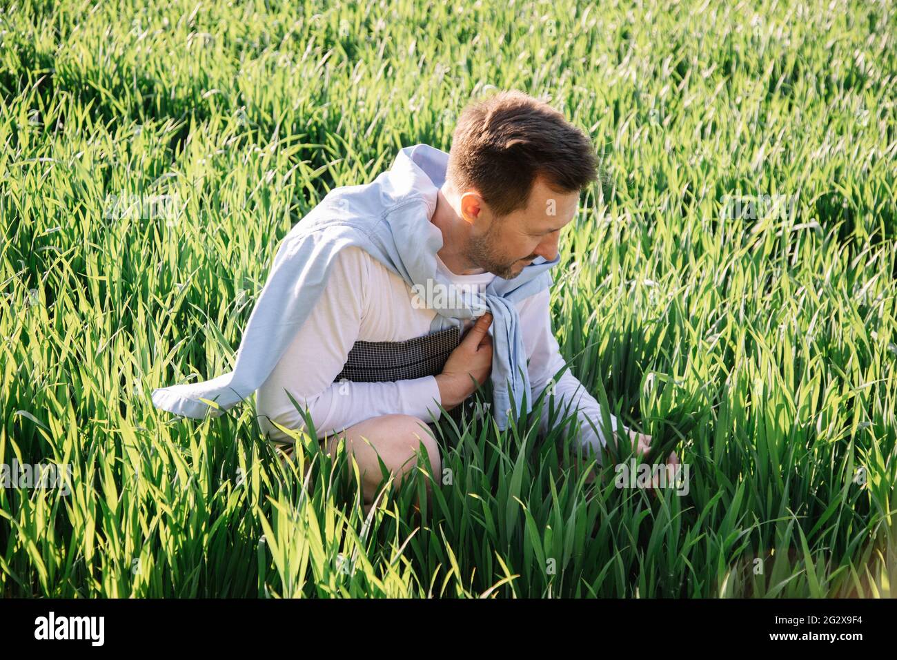 Young farmer with folder under his arm sitting in field 40 years old checking his forage crop, small bussiness concept photo Stock Photo