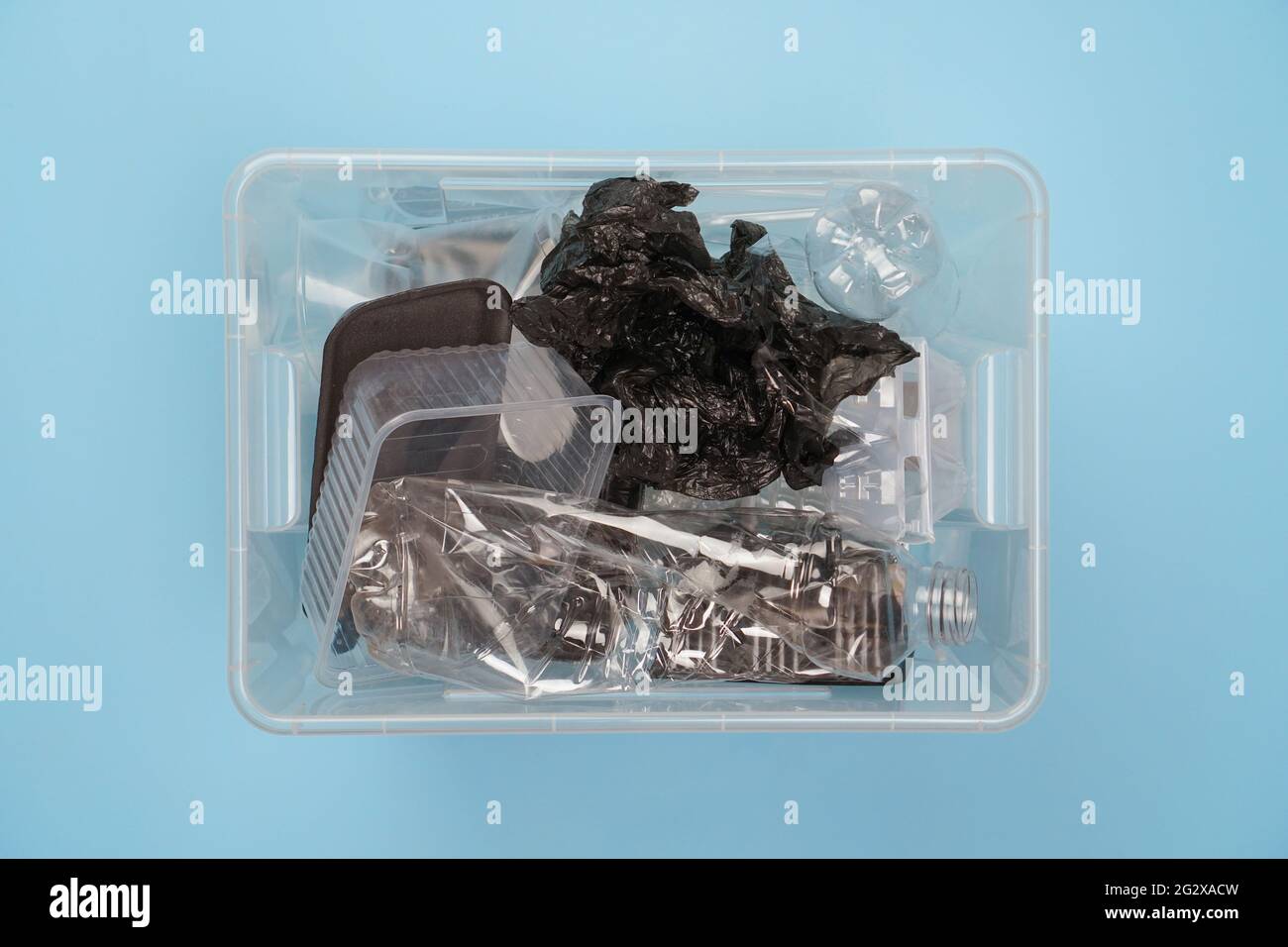 Container with plastic trash: bottles, bags, containers on a blue background. Sorting garbage. Stock Photo