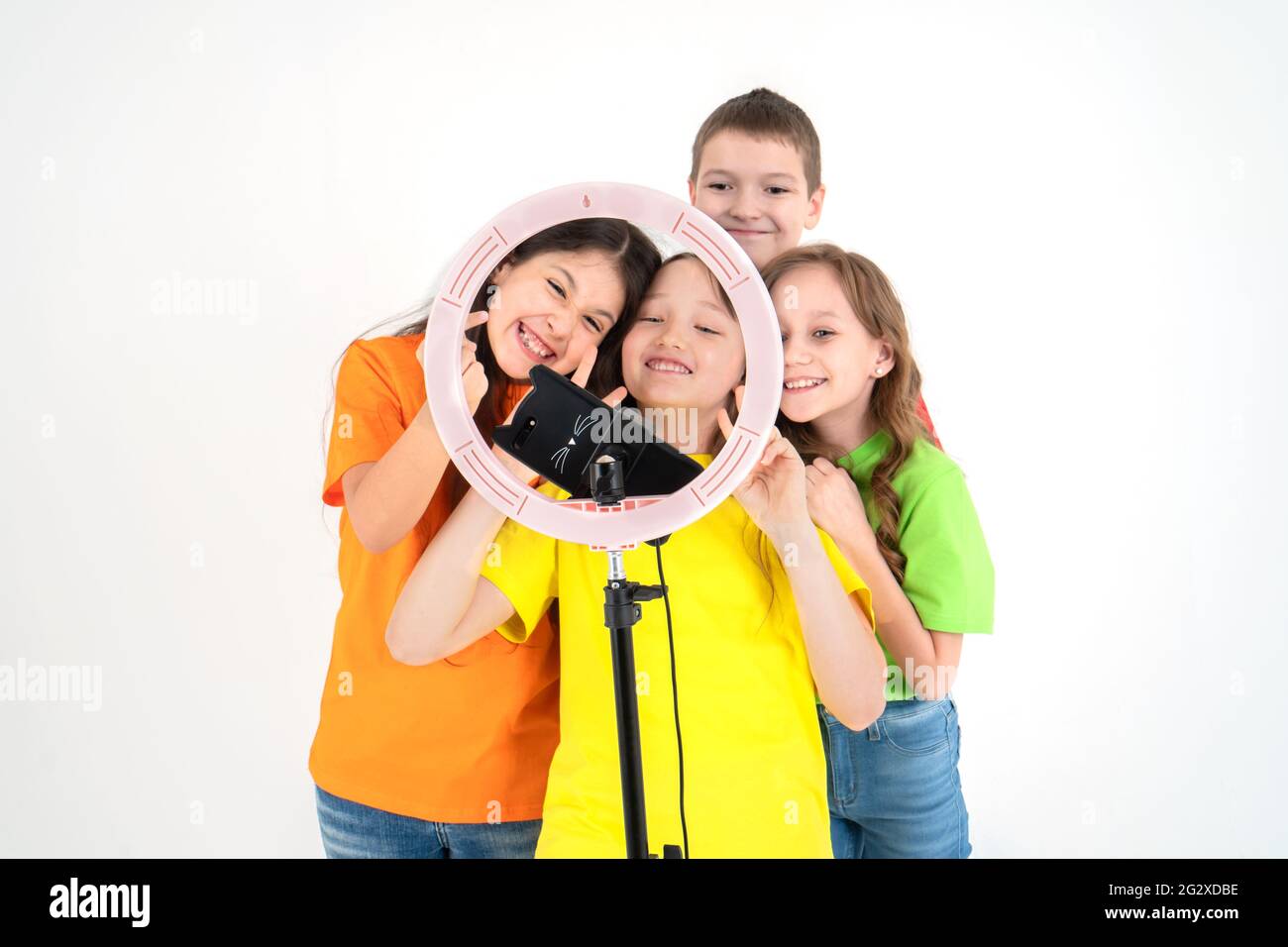 Three teen girls and a boy smiling and shoots a video. Selfies. The phone is mounted on a tripod and the ring lamp shines.Negative emotions and social Stock Photo