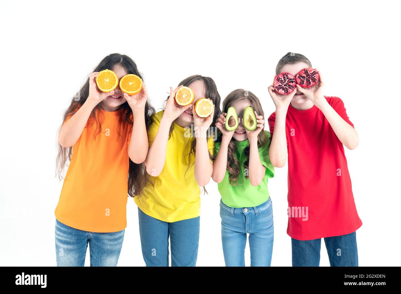 Three girls and a boy using fruits as glasses on a on a white background. Group of happy children with orange, lemon, avocado and pomegranate in hands Stock Photo