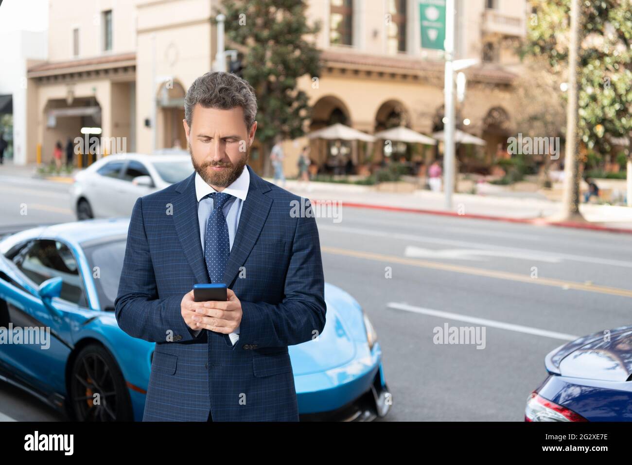 handsome businessman chatting on smartphone stand by luxury auto outdoor. car available. Stock Photo