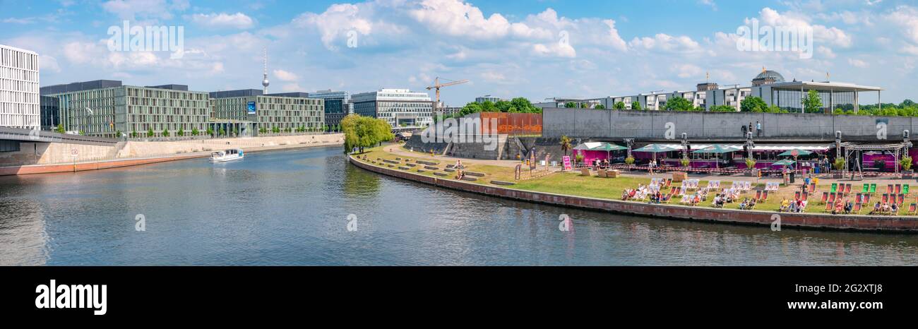 Panoramic view over relaxing people at the cafe Capital Beach at Spree channel, Spreebogen, with a tour boat in historical and business downtown in Be Stock Photo