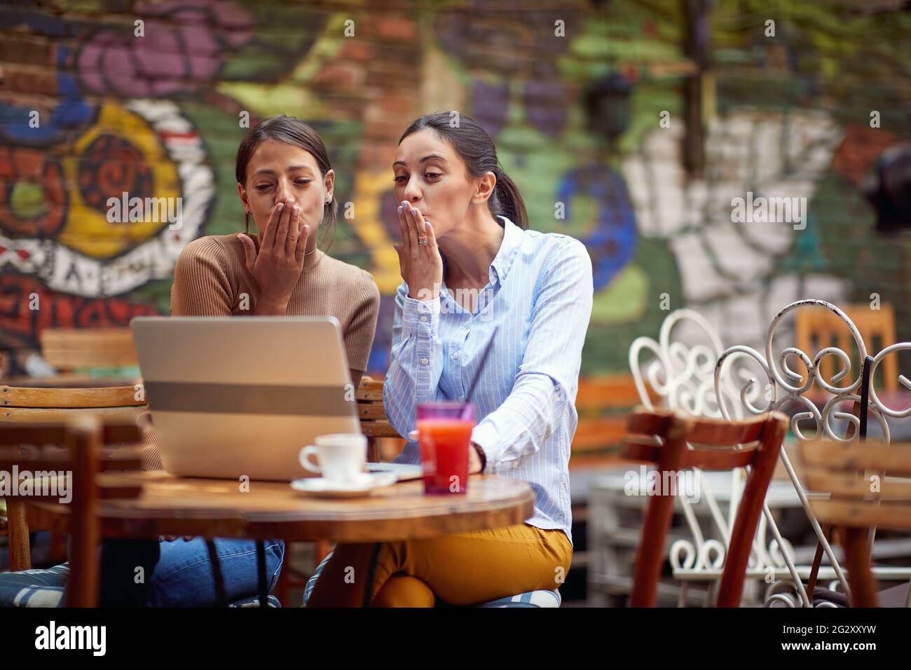 two young adult caucasian females sending kisses to someone online, looking at the laptop Stock Photo