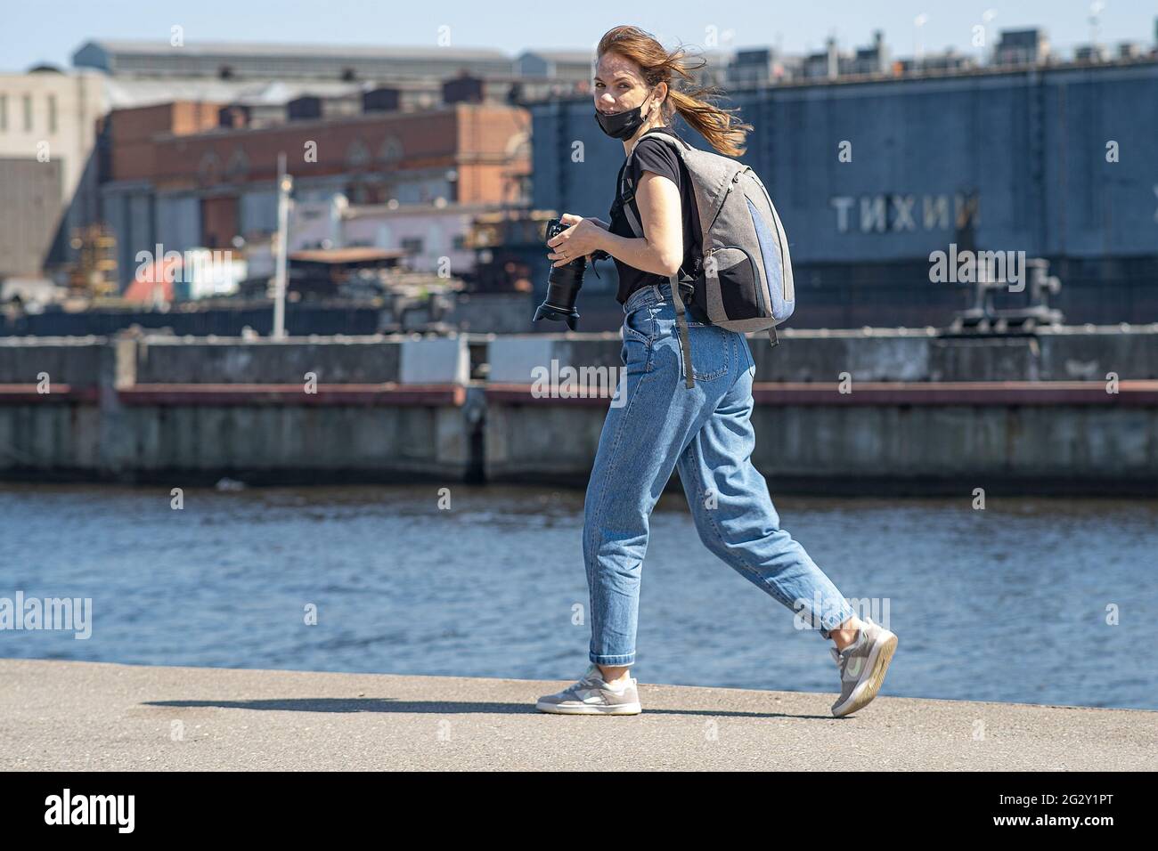 The photographer girl on the pier holds a camera in her hand. As she ran past, she smiled at her colleague's photographer. Saint-Petersburg. Russia. J Stock Photo