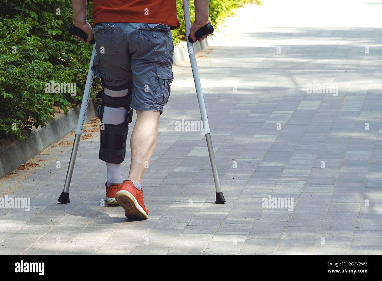 A man with a fixed arch support on the knee joint. With difficulty, he walks on the cobblestones with the help of crutches. The concept of health, phy Stock Photo