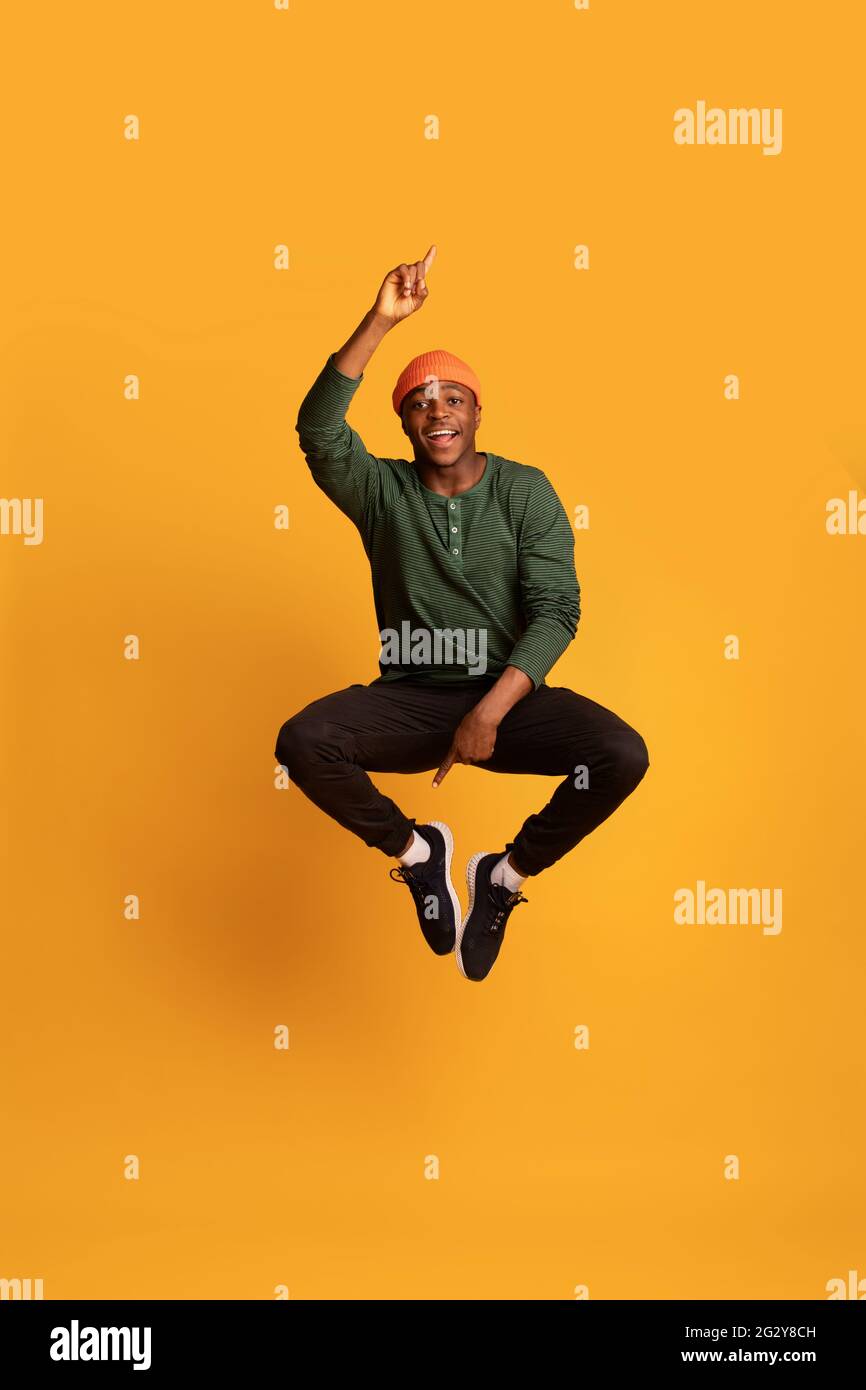 Check This. Cheerful Young Black Guy Pointing Up And Down While Jumping Stock Photo