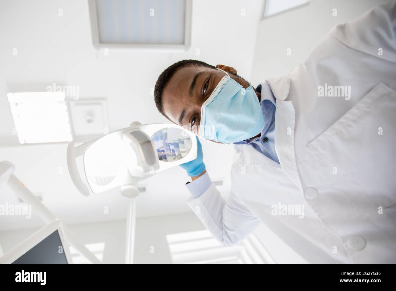 Black Stomatologist Turning On Lamp Before Check Up With Patient, Low Angle Stock Photo