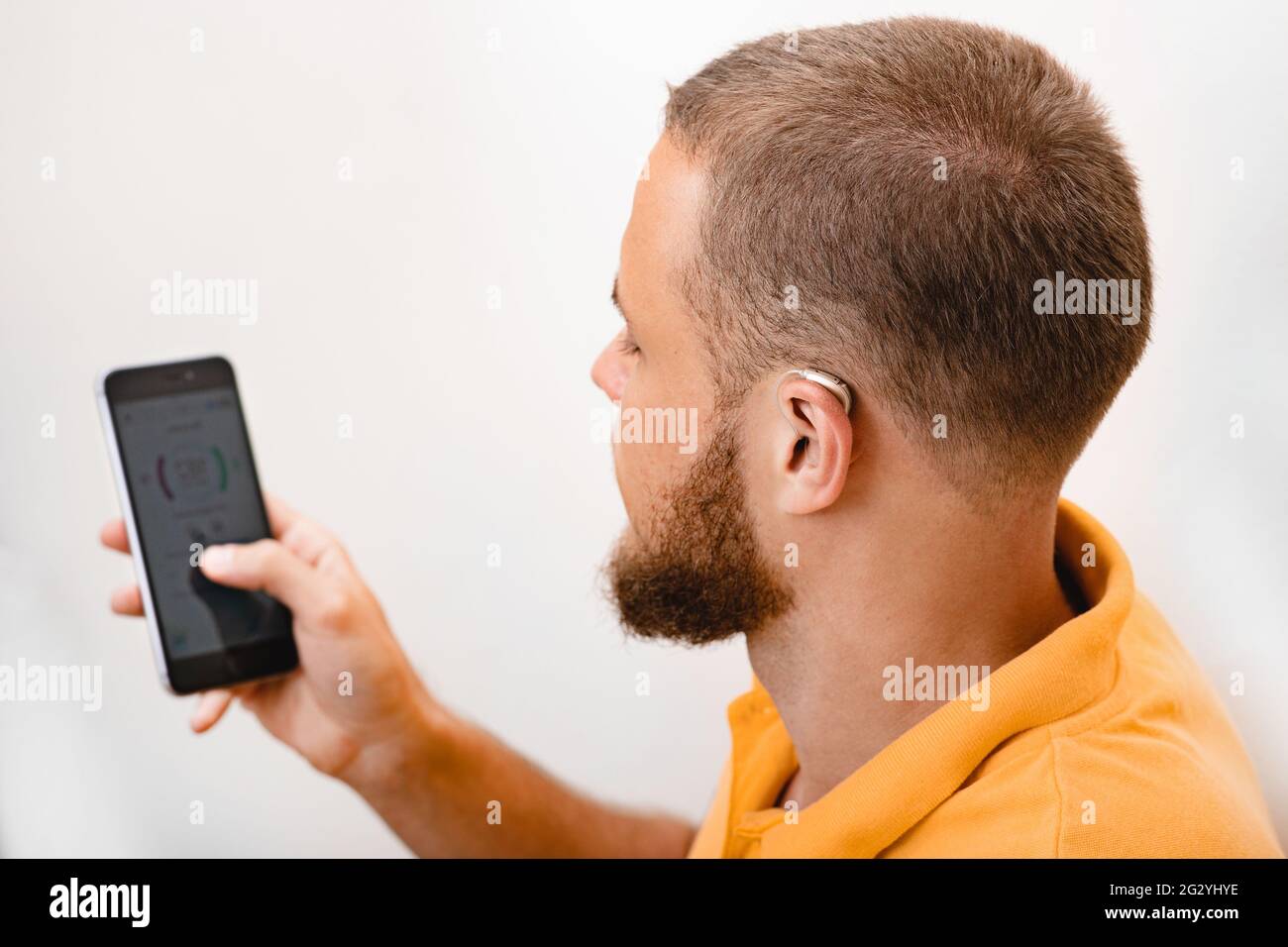 Hearing impaired man adjusts settings for his BTE hearing aid via smartphone. Hearing aids, deafness treatment, innovative technologies at audiology Stock Photo