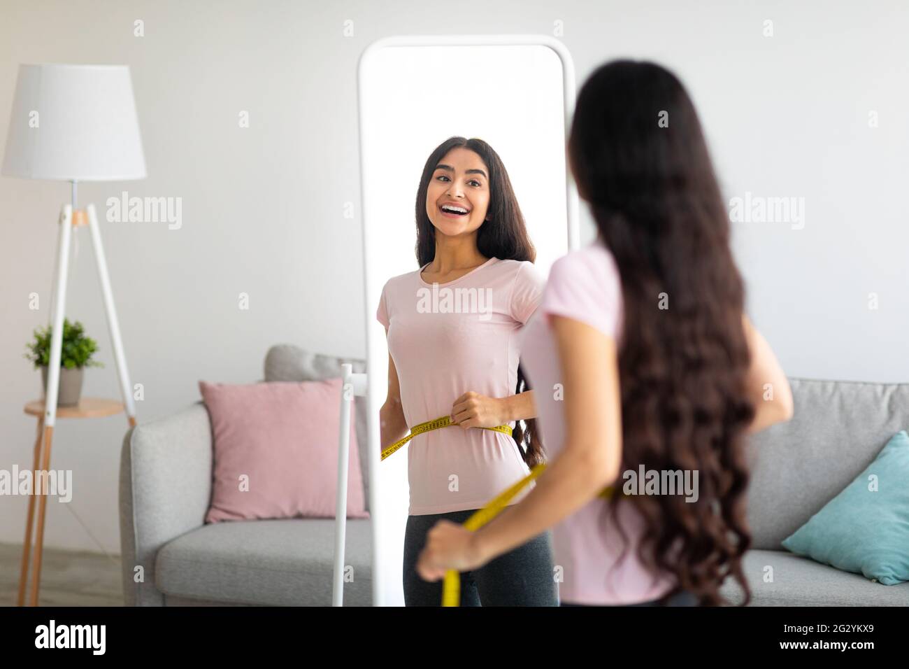 Attractive young Indian woman measuring her waist with tape near mirror indoors, copy space Stock Photo