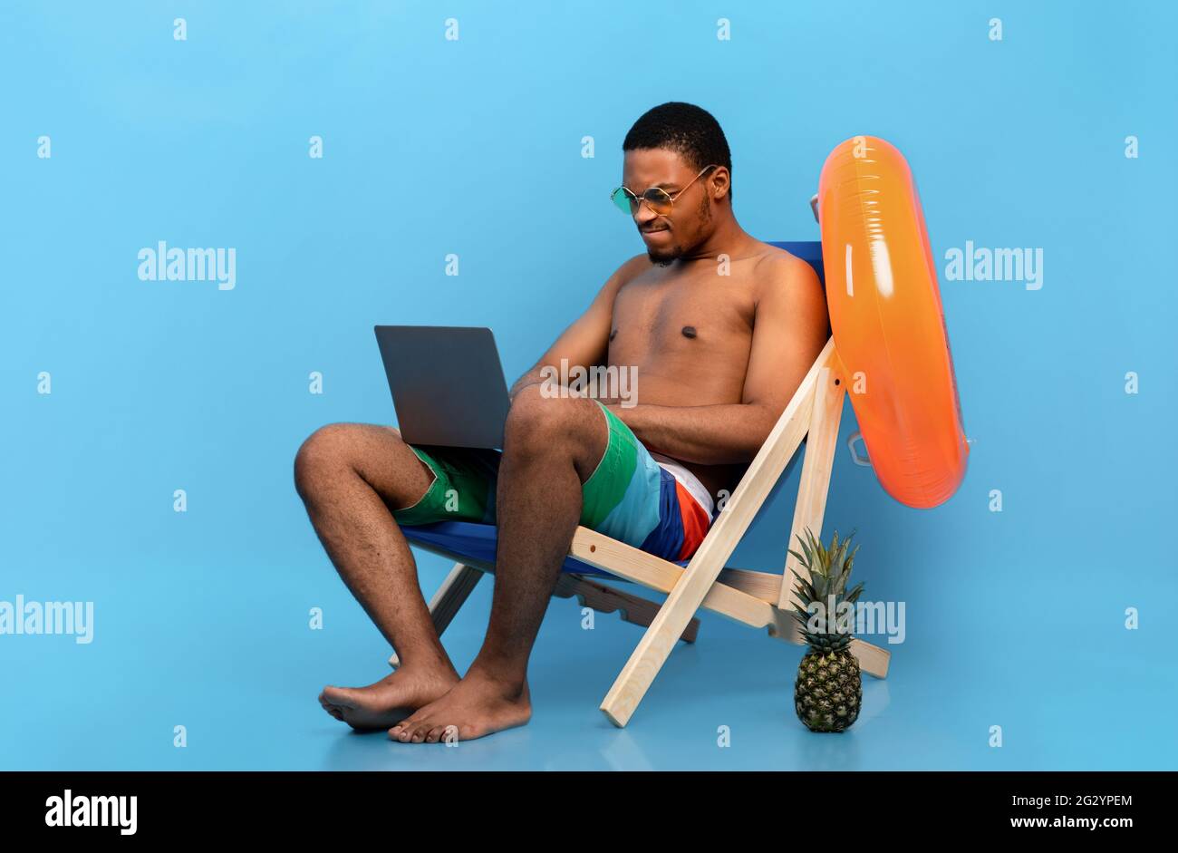Computer problems. Frustrated black guy having trouble with laptop while sitting in lounge chair on summer vacation Stock Photo