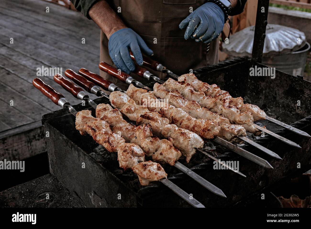 The chef prepares chicken shish kebab. Street food. Meat cooked over a fire, BBQ party in the backyard. Male hands in gloves hold steel skewers with d Stock Photo
