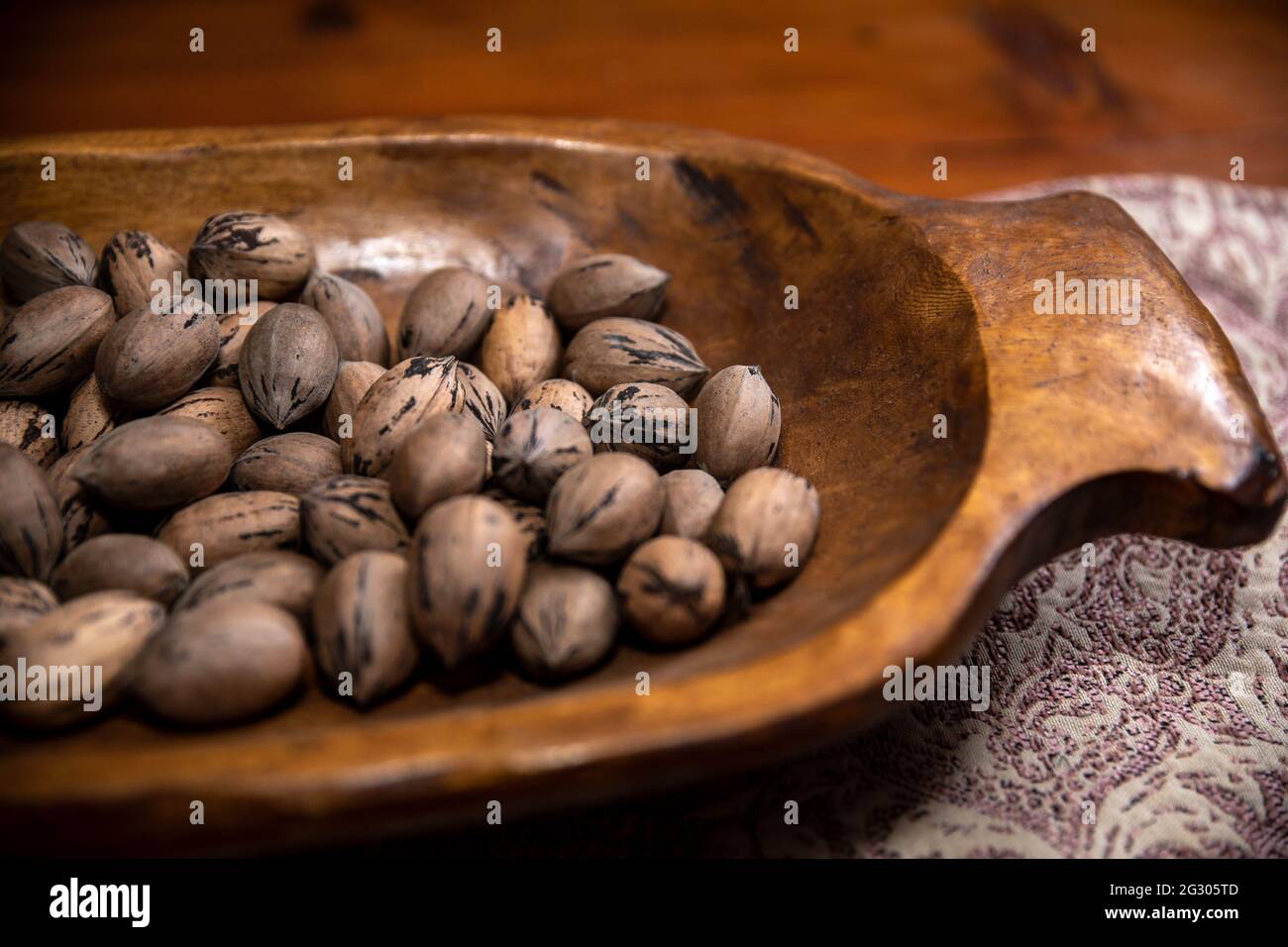 Raw in shell whole Pecan nuts in a wooden bowl on a wood table Stock Photo