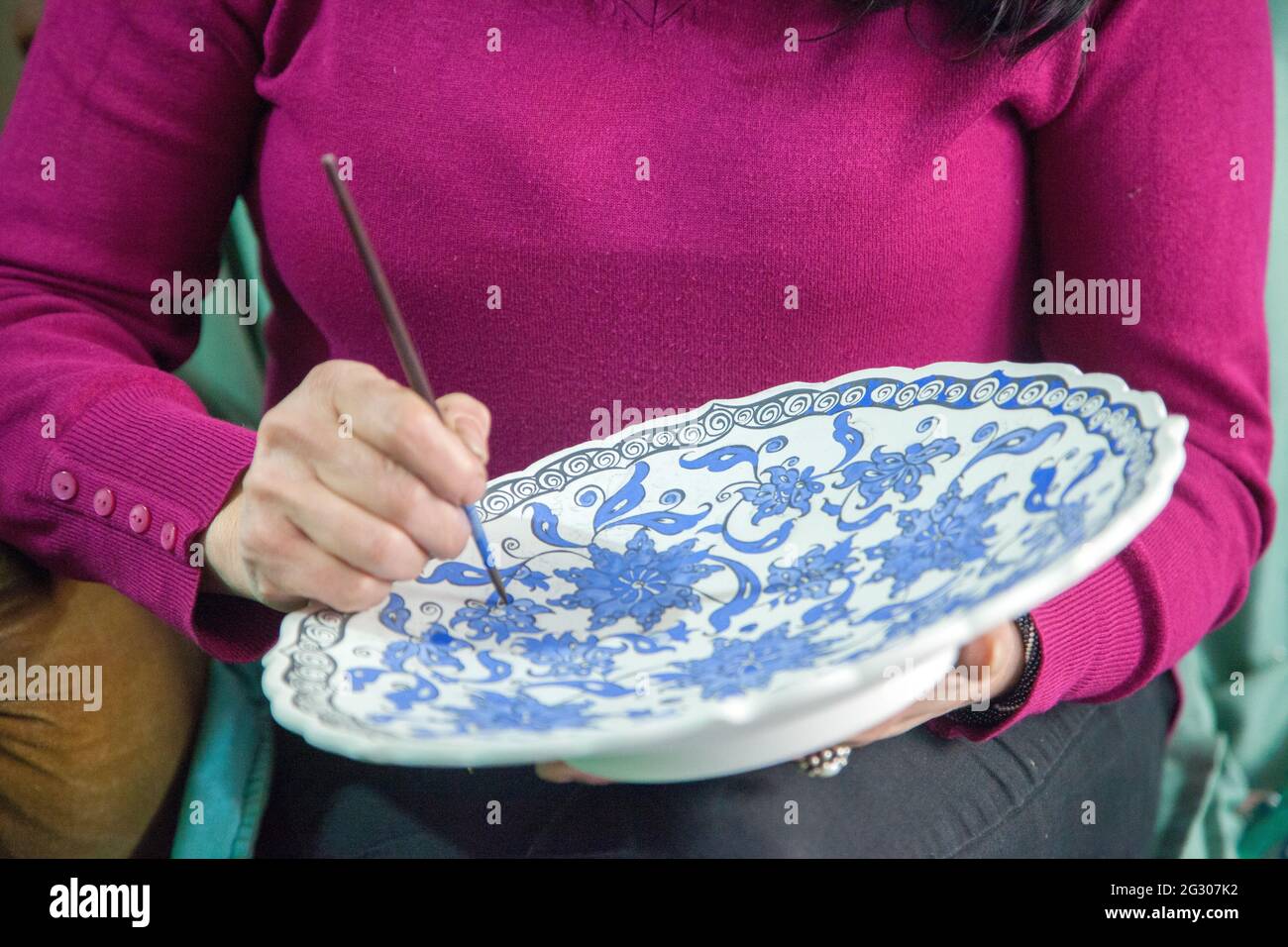 Female tile artist paints porcelain at workshop. Izmik, Turkey. 30 December 2016 Stock Photo