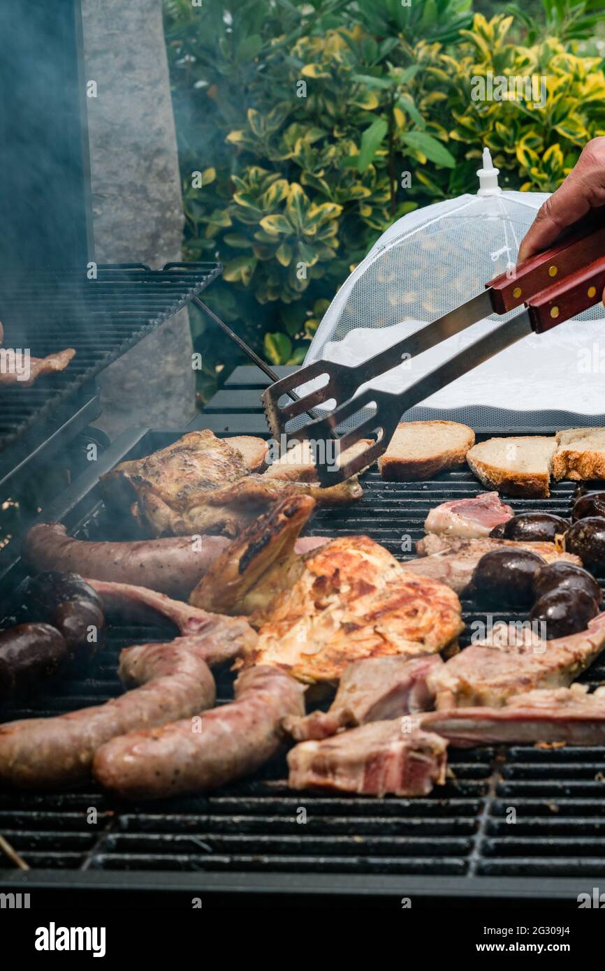 Man grilling meat on a barbecue various types of meat, chicken, sausages, blood sausage, lamb on a crbon grill in the garden Stock Photo