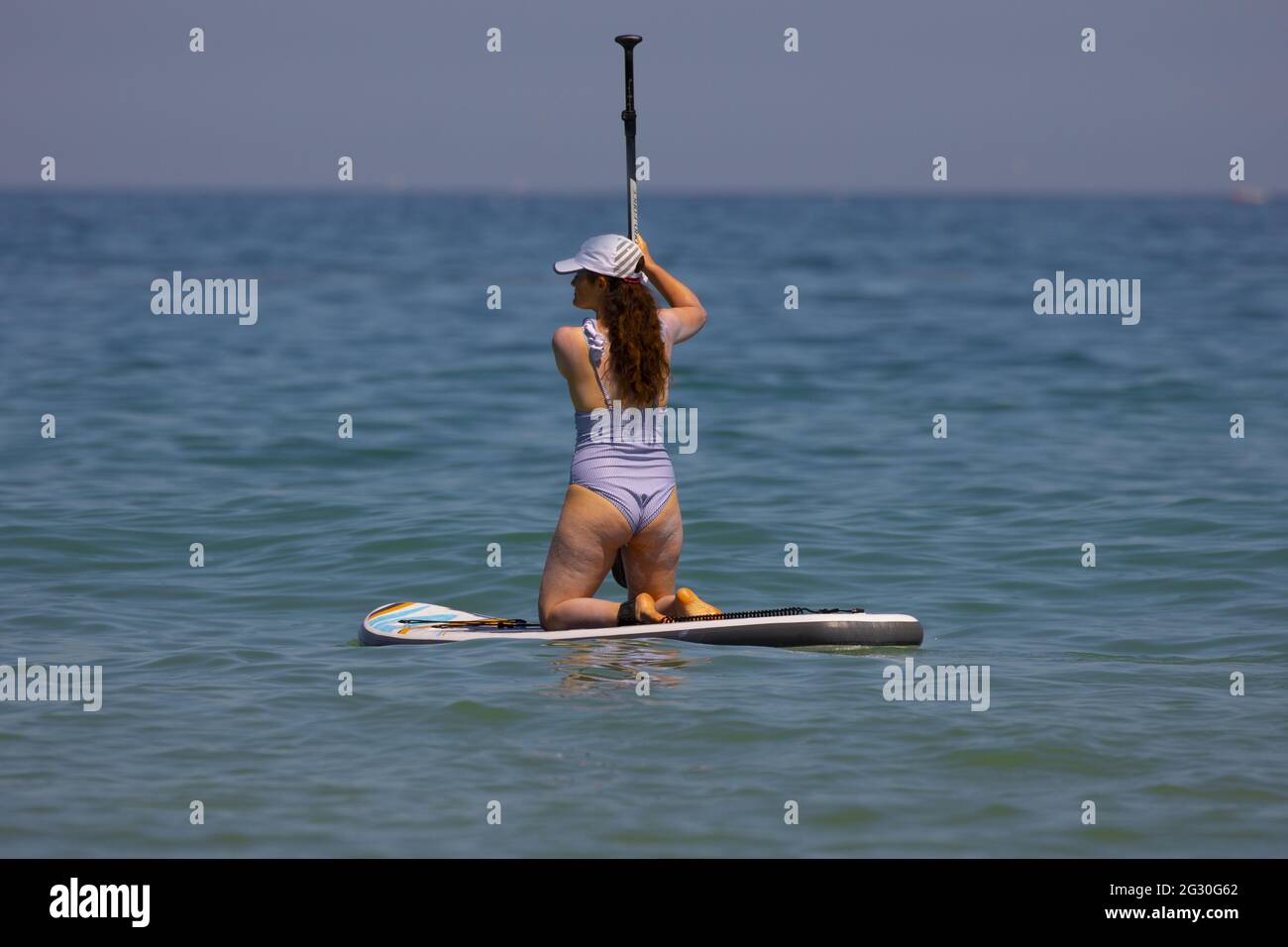 Harlyn Bay, Cornwall, UK. Sunday 13th June 2021, UK Weather:  The hottest day of the year so far with many people hitting the beach to call off in the sea.  A young female paddleboarder in the sea at Harlyn Bay, Cornwall © DGDImages/Alamy Live News Stock Photo