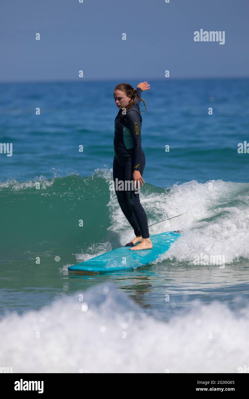 Harlyn Bay, Cornwall, UK. Sunday 13th June 2021, UK Weather:  The hottest day of the year so far with many people hitting the beach to call off in the sea. A female surfer hitting the waves at Harlyn Bay, Cornwall on the hottest day of the year  © DGDImages/Alamy Live News Stock Photo