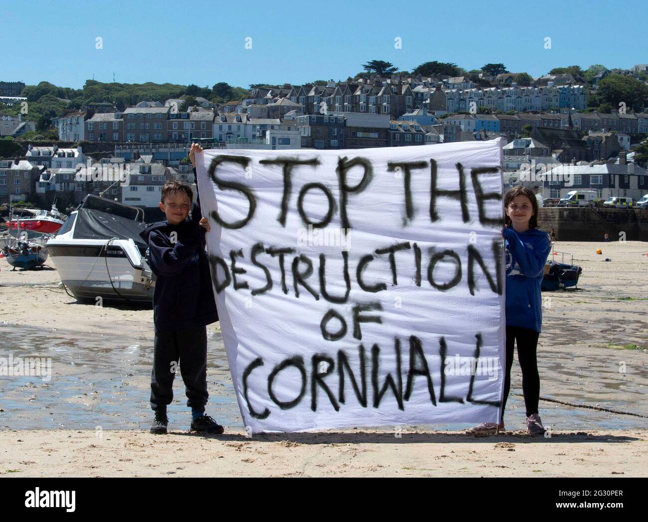 St Ives, Cornwall, UK. 13th June, 2021. Two young members of Extinction Rebellion hold a banner in front of St Ives harbour, close to Carbis Bay Hotel which is hosting the G7 summit. 13th June 2021. Anna Hatfield/ Pathos Credit: One Up Top Editorial Images/Alamy Live News Stock Photo