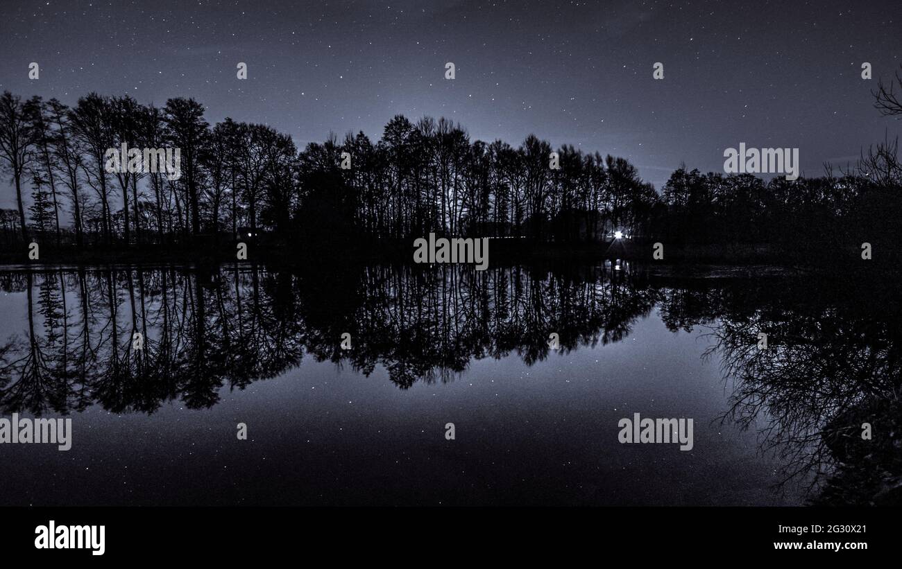 Small lake surrounded by trees reflecting the stars on the night sky ...