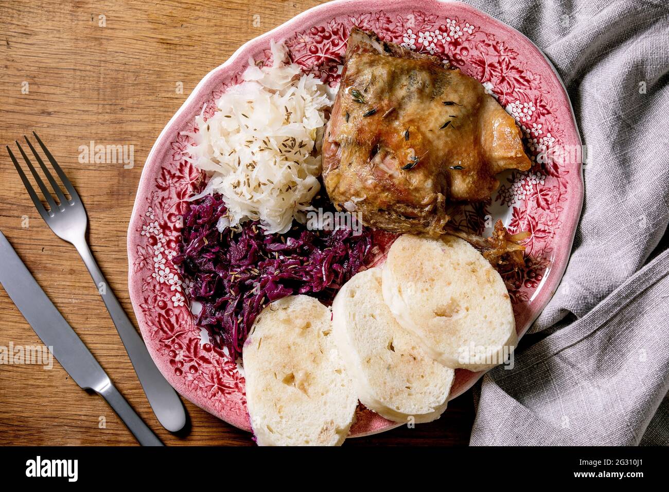 Baked duck legs with sliced boiled bread knedliks, sauerkraut in ceramic plate, decorated with napkin over brown wooden background. Traditional Czech, Stock Photo
