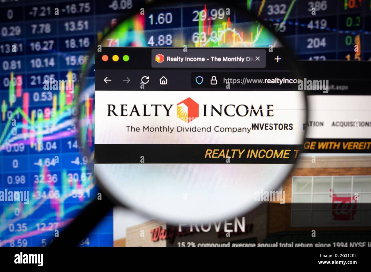 Realty Income company logo on a website with blurry stock market developments in the background, seen on a computer screen through a magnifying glass Stock Photo