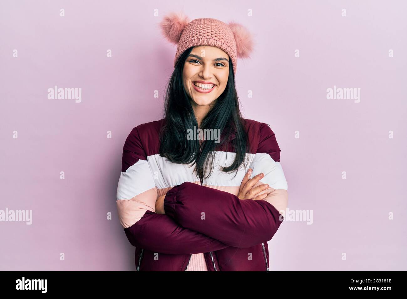 Young hispanic woman wearing wool winter sweater and cap happy face smiling with crossed arms looking at the camera. positive person. Stock Photo