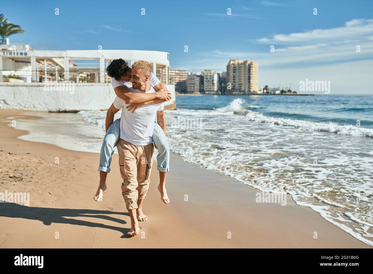 Lovely gay couple on piggyback ride at the beach. Stock Photo