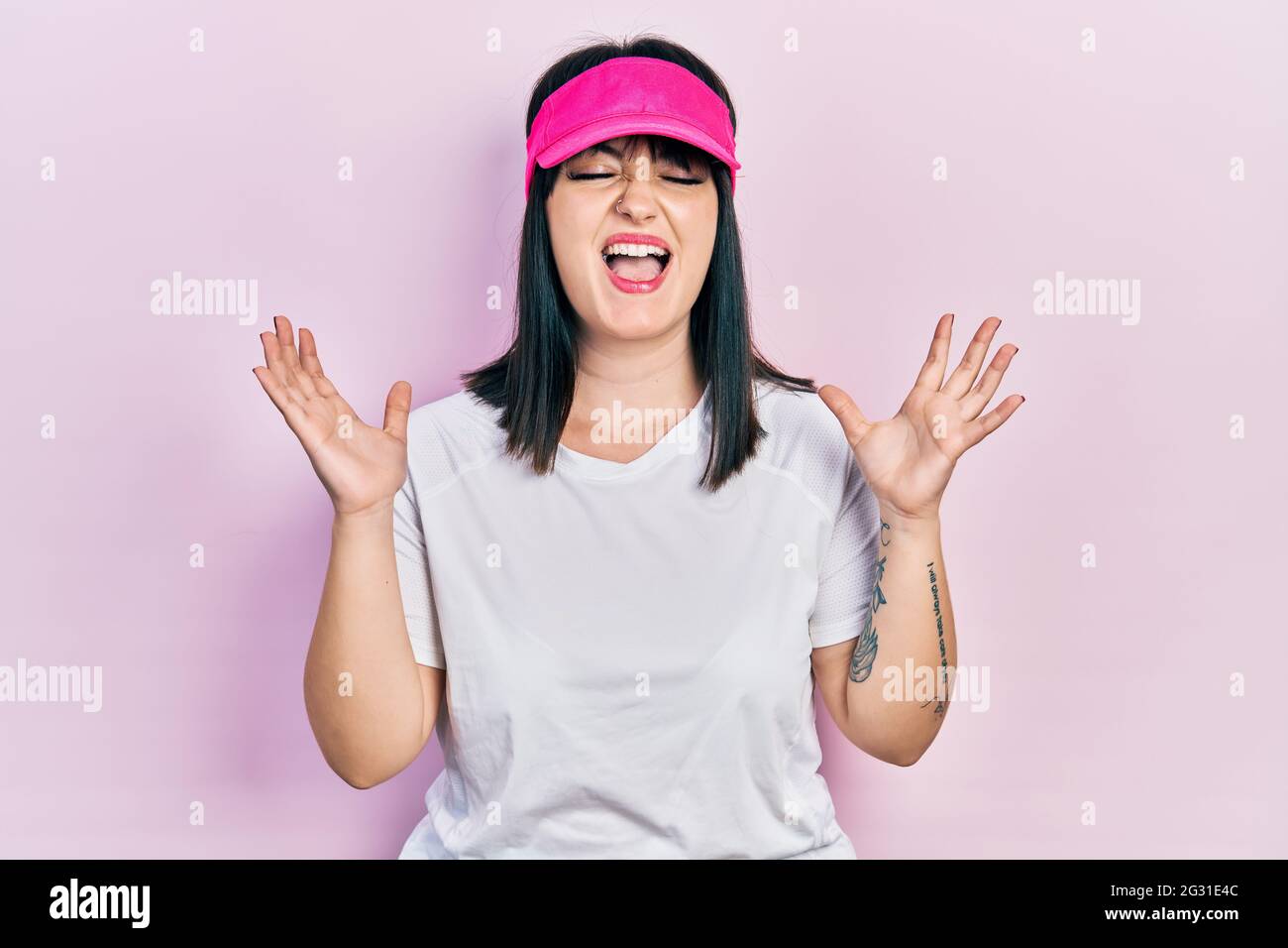 Young hispanic woman wearing sportswear and sun visor cap celebrating mad and crazy for success with arms raised and closed eyes screaming excited. wi Stock Photo