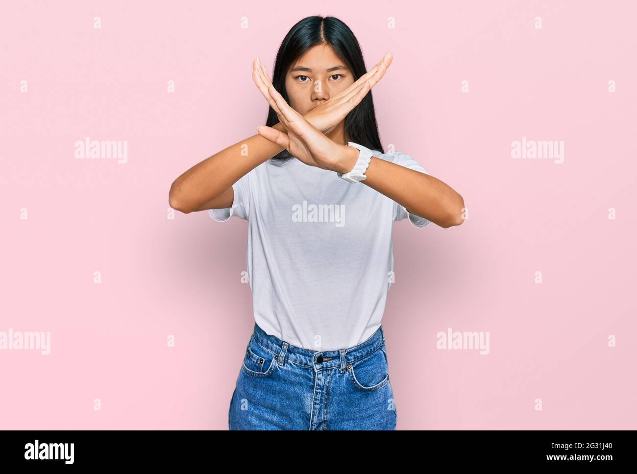 Beautiful young asian woman wearing casual white t shirt rejection expression crossing arms and palms doing negative sign, angry face Stock Photo