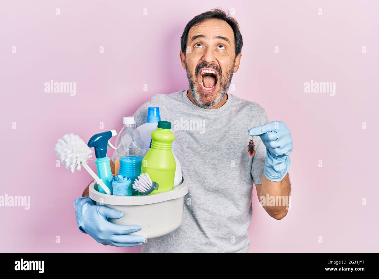 Middle age hispanic man holding cleaning products holding cockroach ...