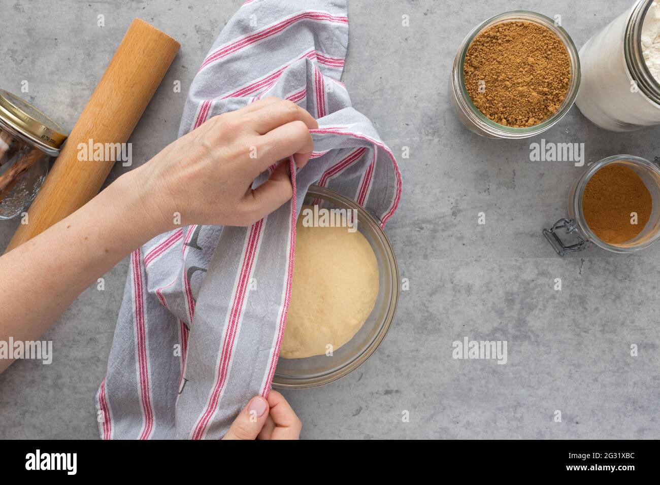 Woman hands covering a cinnamon roll dough with a kitchen cloth for rising. Stock Photo