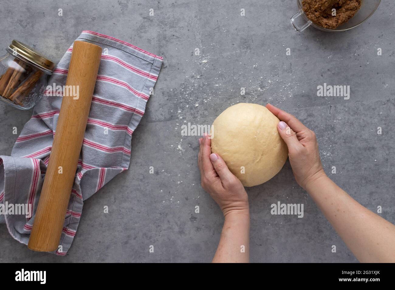 Woman hands handling a rounded dough on a grey rustic table with some flour powder sprinkled on it. Stock Photo