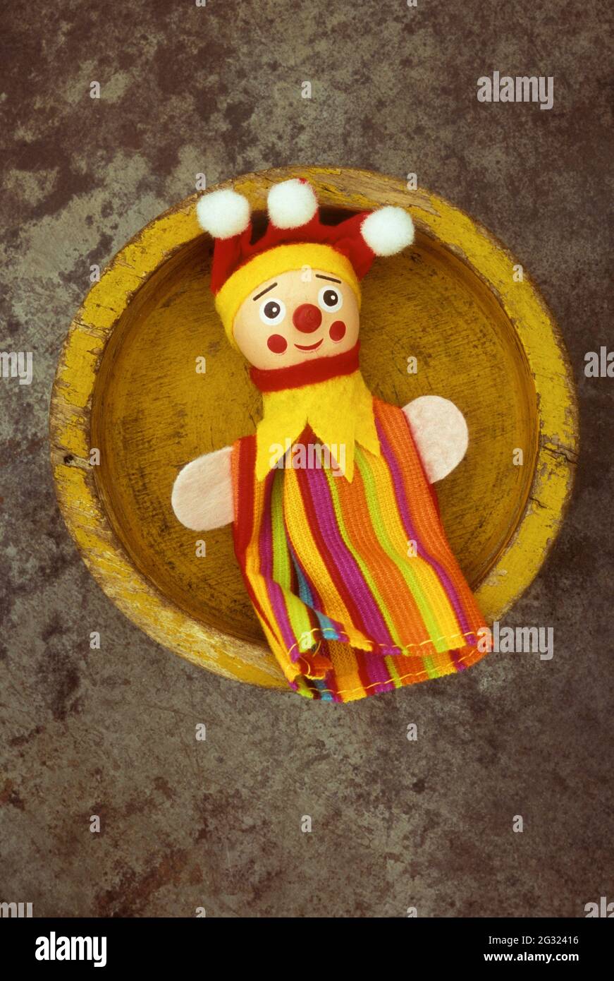 Old yellow wooden dish containing puppet or doll with round wooden head worried look and jester clothes Stock Photo