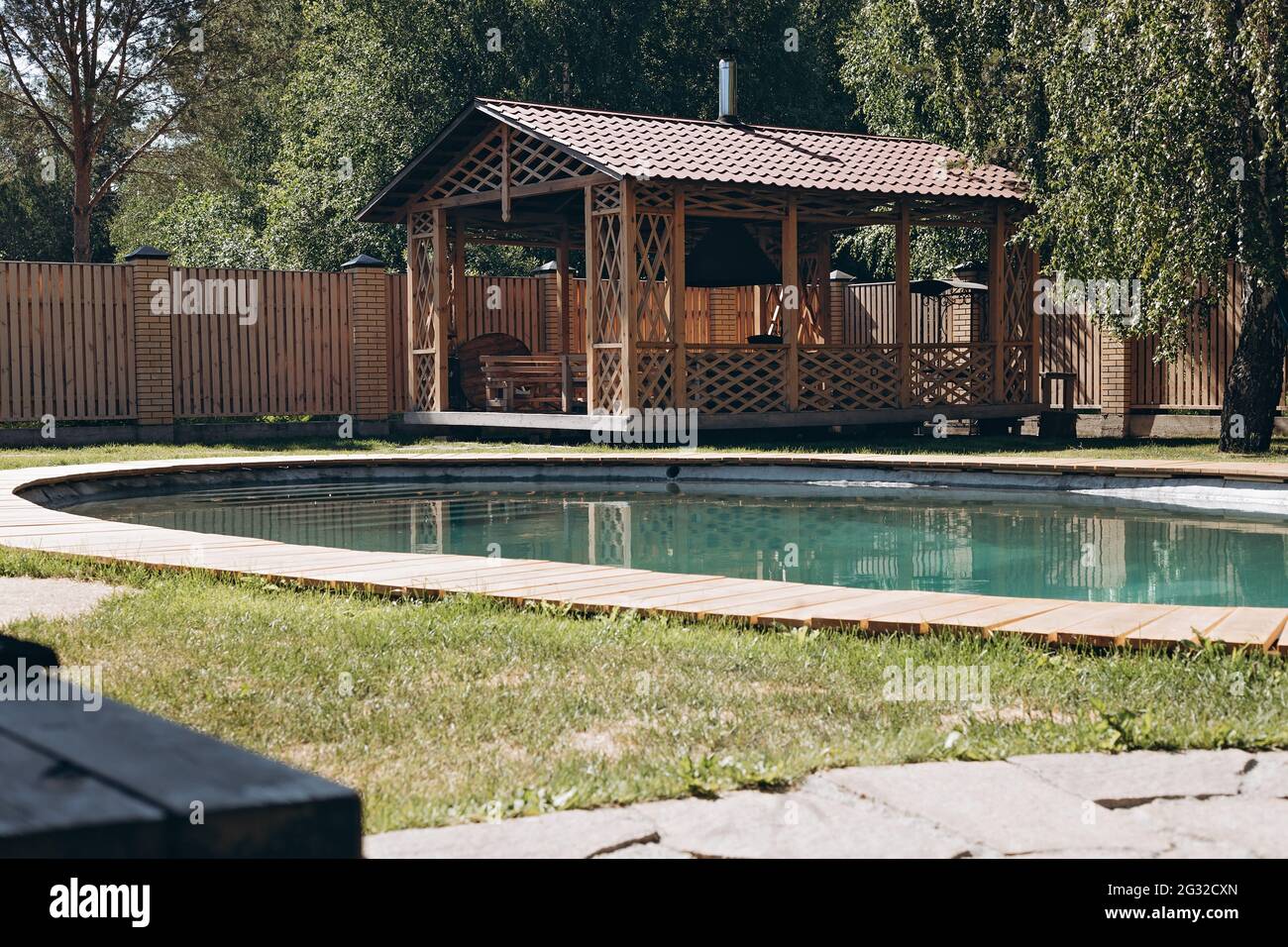 Wooden barbecue gazebo, patio area and swimming pool in backyard of