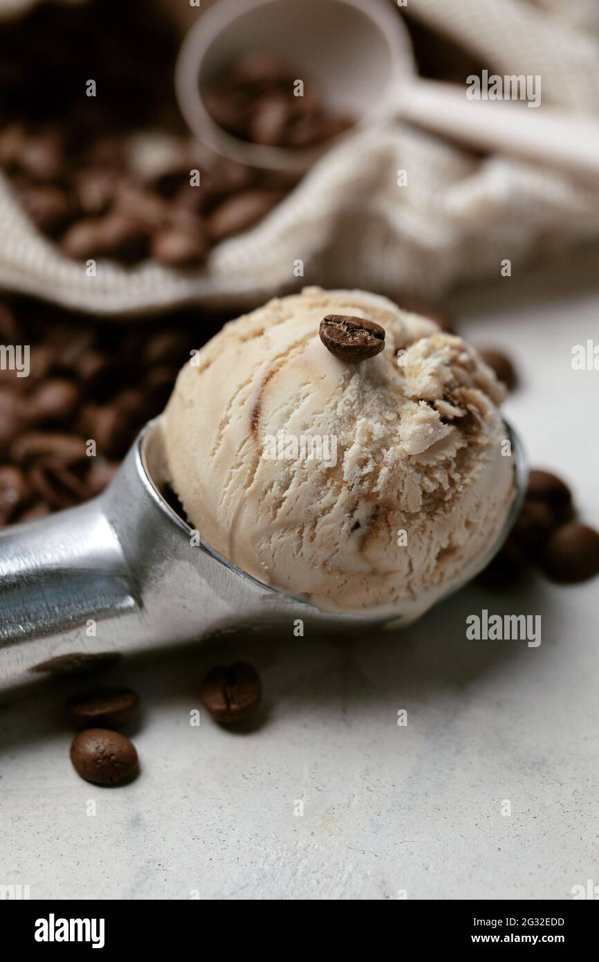 Silver scoop with coffee ice cream and coffee beans on white clay