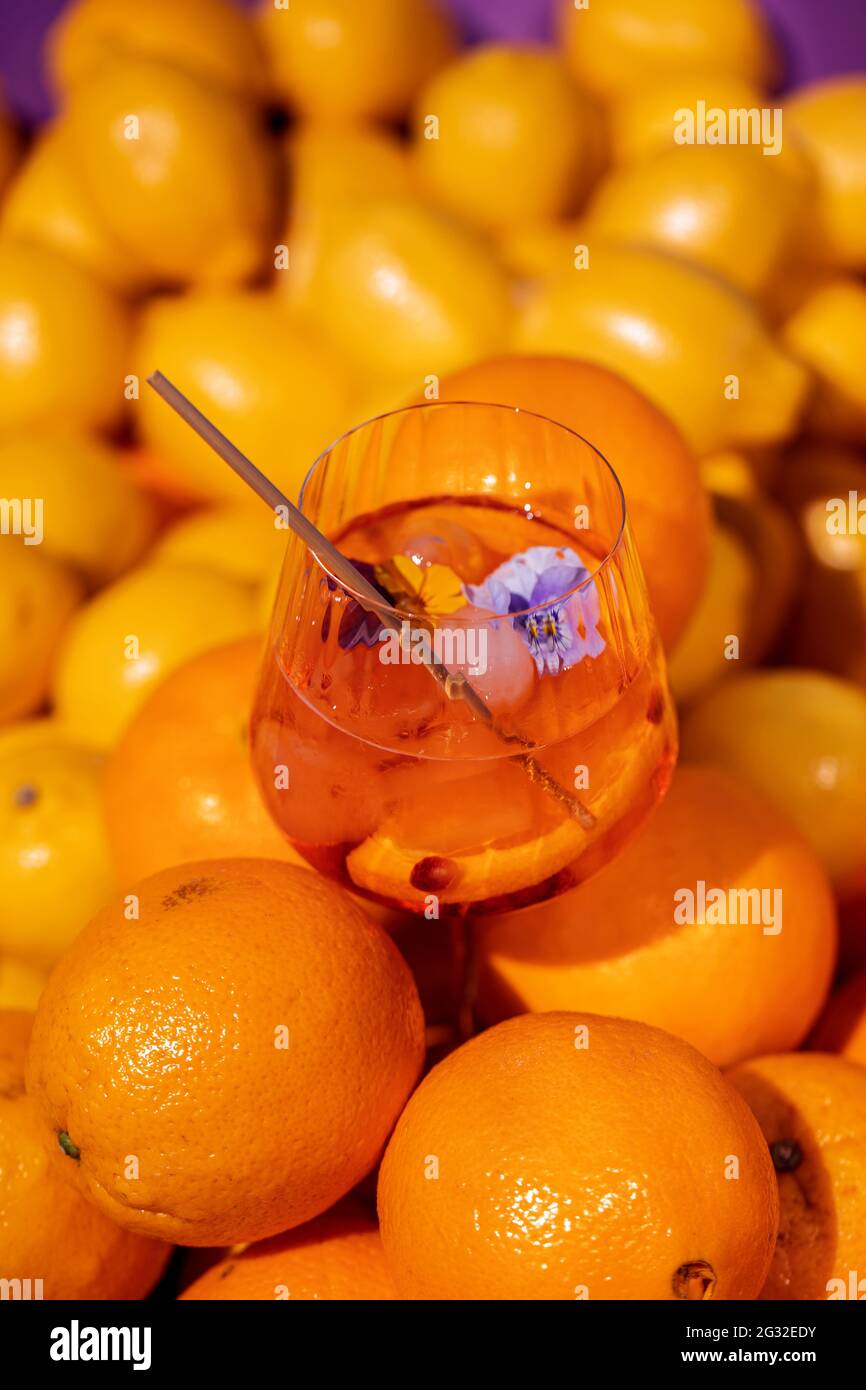 Summer refreshment aperitif cocktail in wine glass with ice rocks, bamboo straw and sliced oranges in fresh oranges and limes background Stock Photo