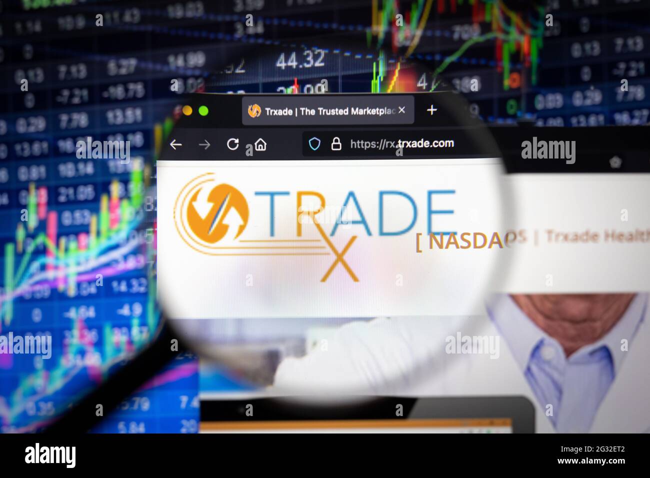 Trxade company logo on a website with blurry stock market developments in the background, seen on a computer screen through a magnifying glass Stock Photo