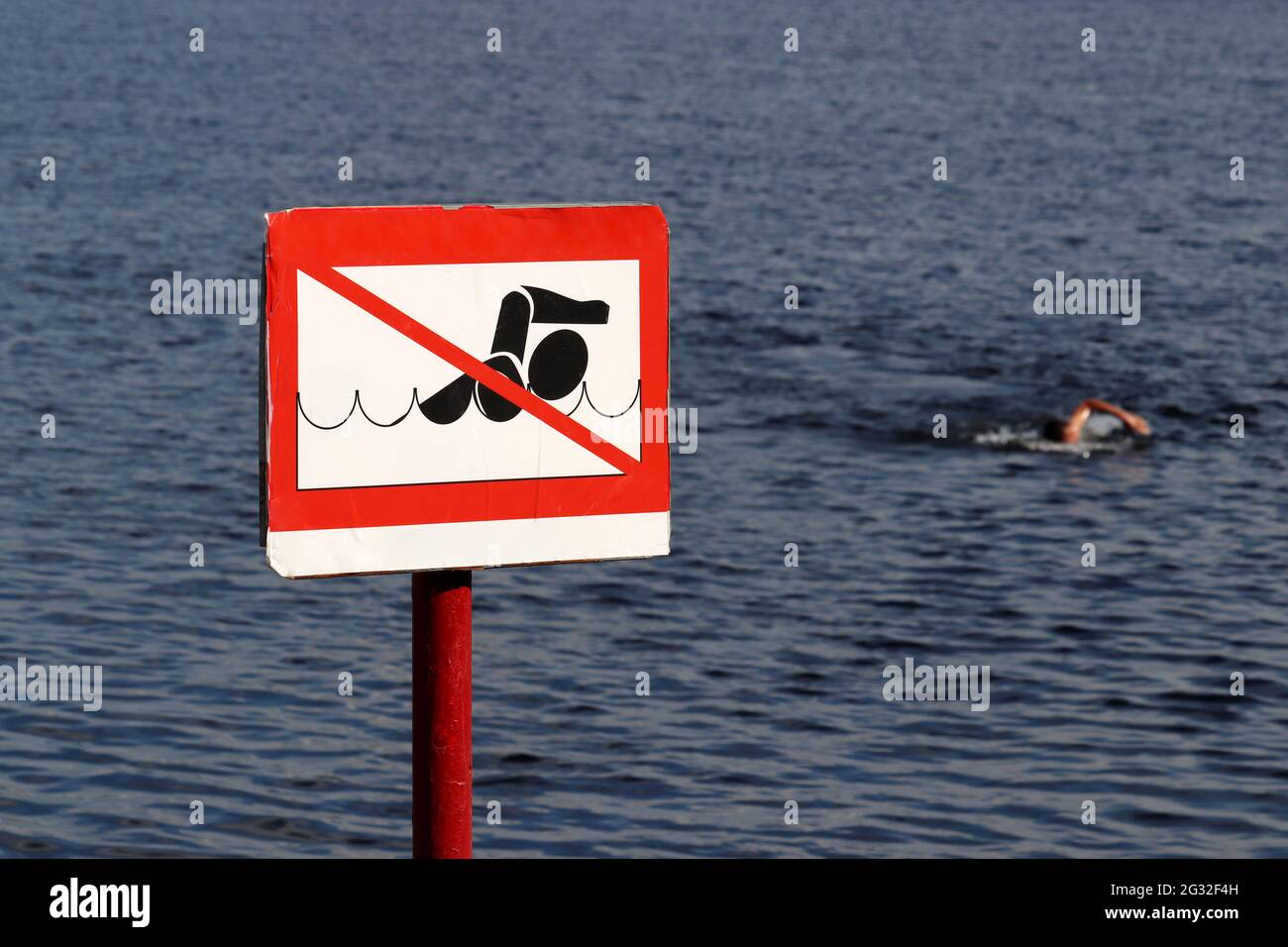 No swimming sign on background of sea and swimmer. Beach holiday on summer sea or river Stock Photo