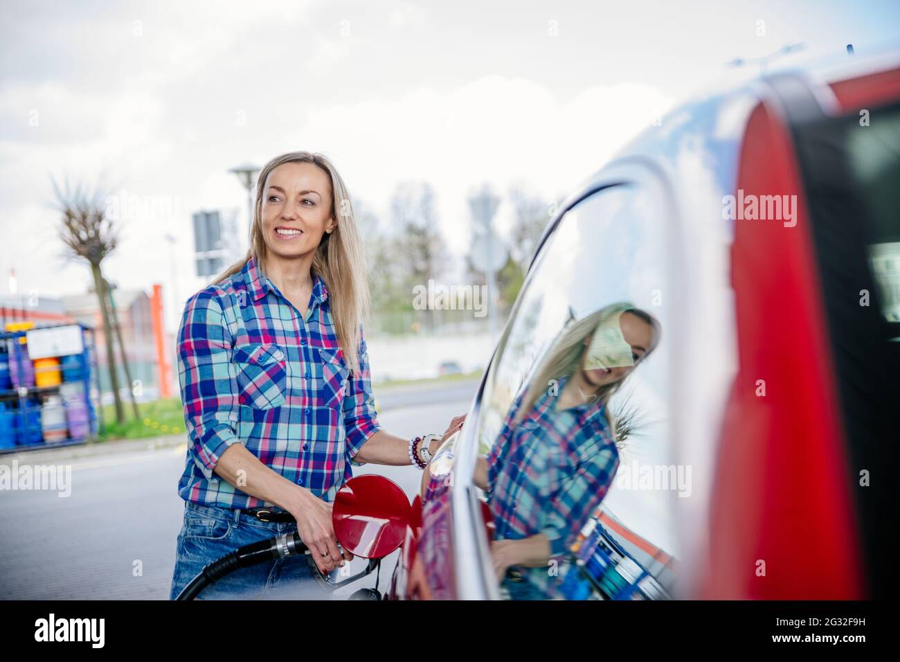 Pretty blonde fills her red car with gasoline at the gas station Stock Photo