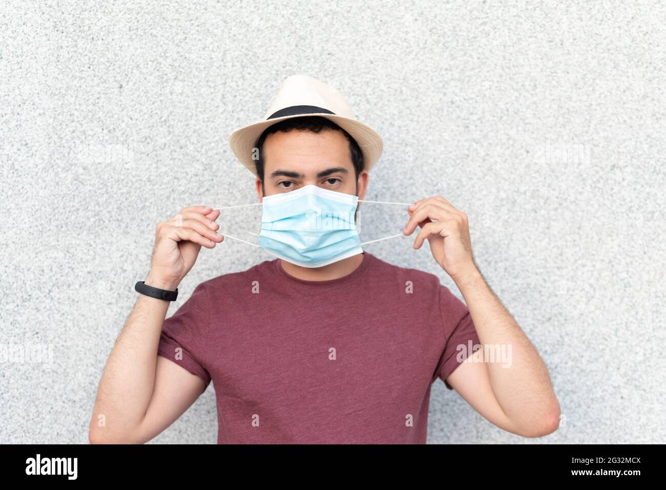 Young man with hat putting on blue mask Stock Photo - Alamy