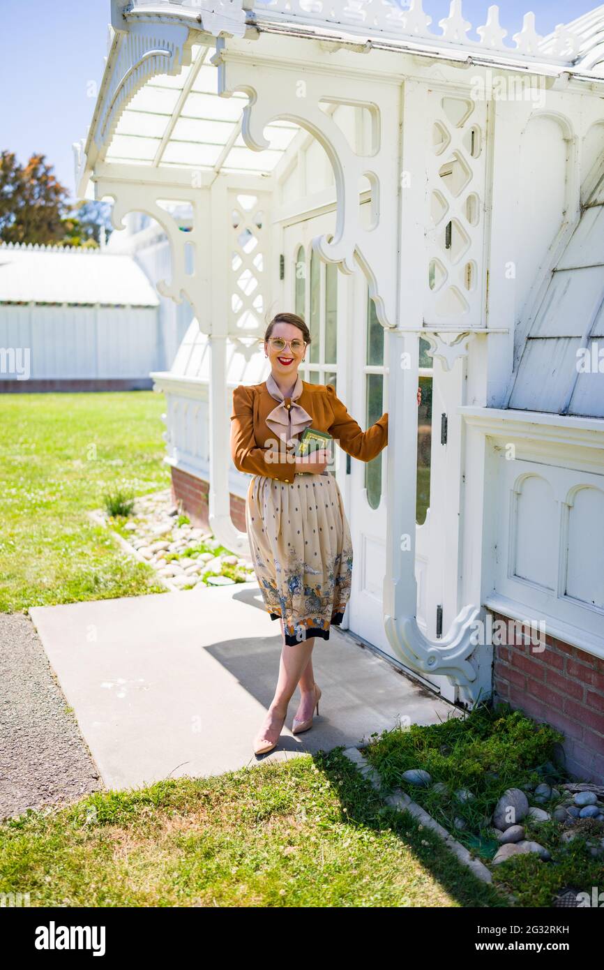 Young Woman in 1940s Fashion Standing in Front of Victorian Conservatory Stock Photo