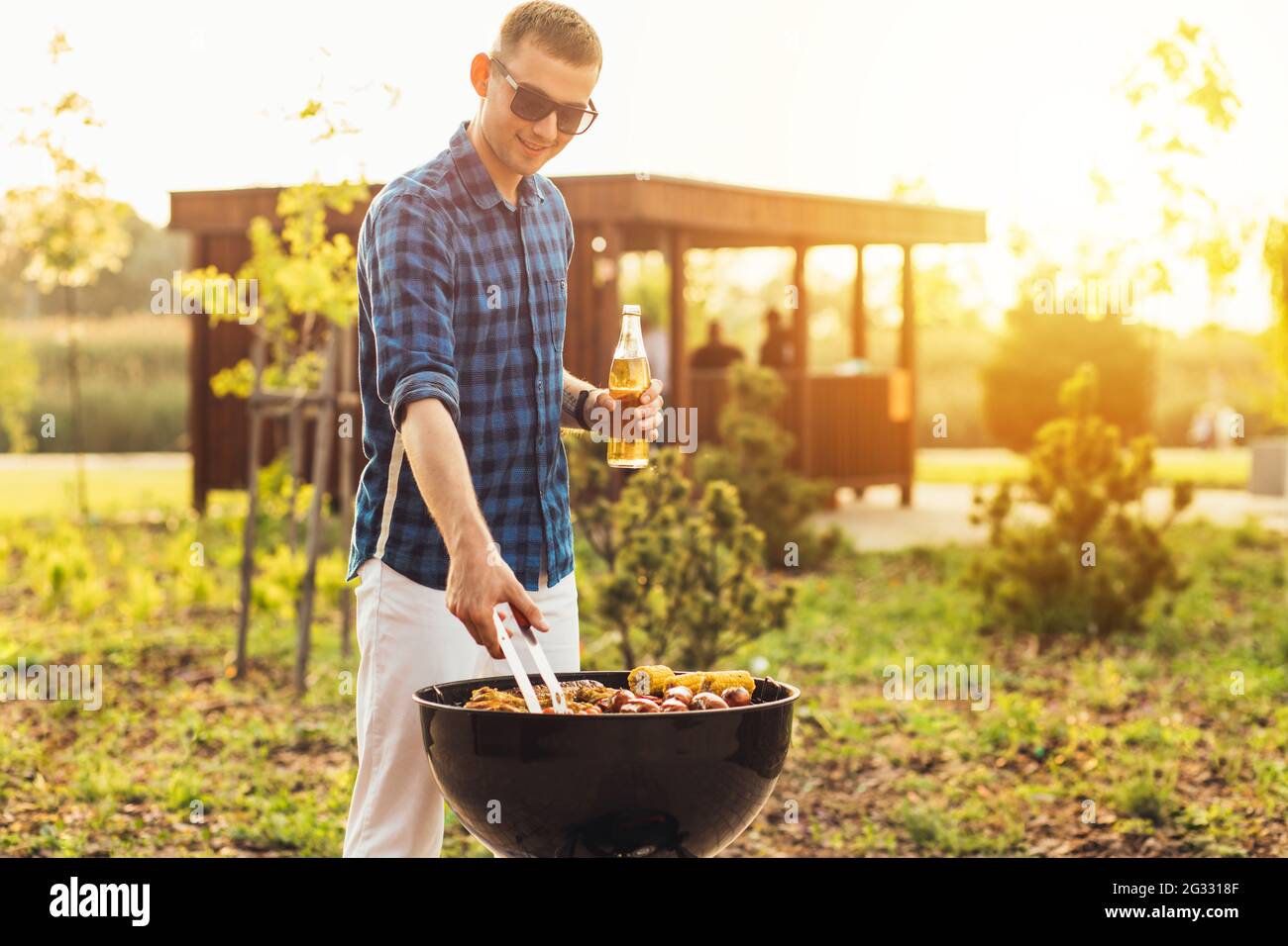 Man making barbecue, assorted vegetables and chicken wings with sausages, grilling on a portable barbecue outdoors in a park in nature Stock Photo