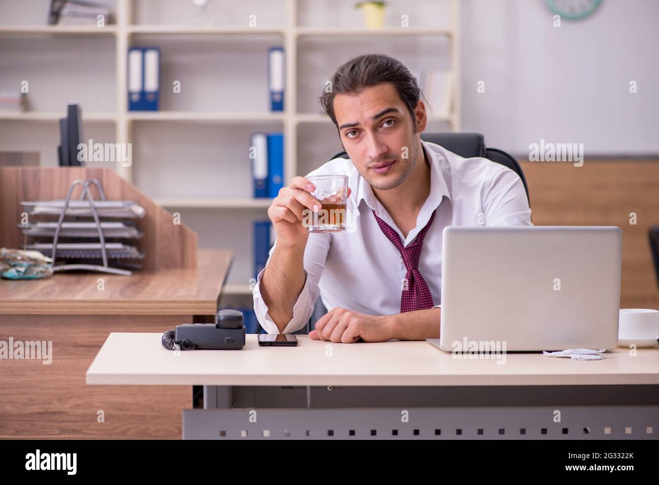Young employee drinking alcohol in the office Stock Photo - Alamy
