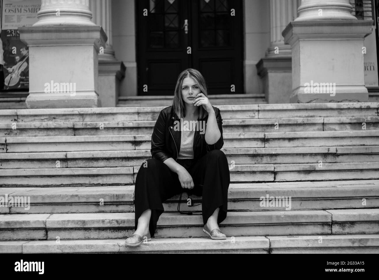 A grayscale shot of an attractive stylish female sitting on stairs and posing in the city Stock Photo