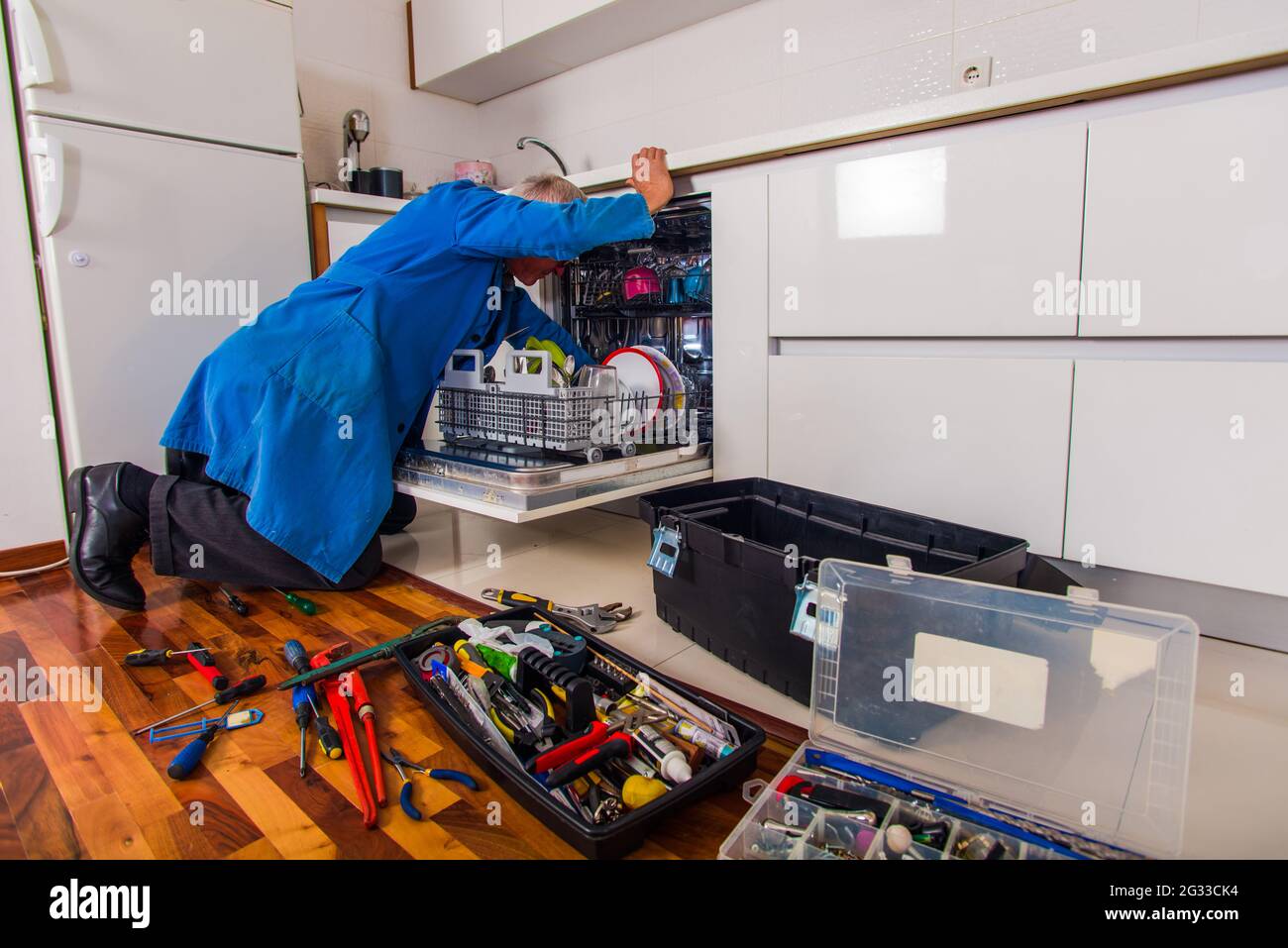 Mature handyman is opening the dishwasher in the kitchen with the tool