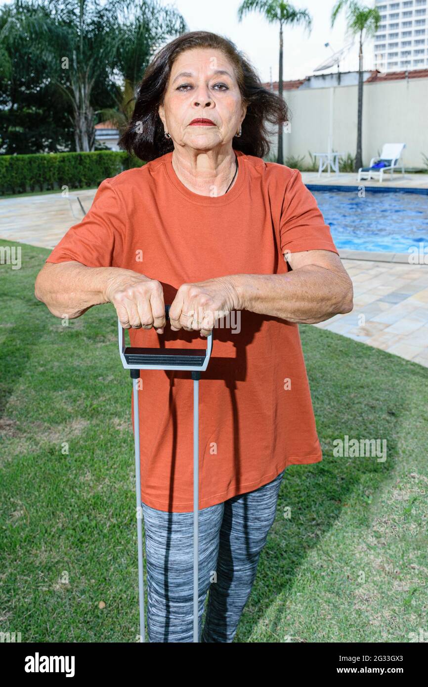 74 years old woman doing exercises with rubber band on the edge of the pool. Stock Photo