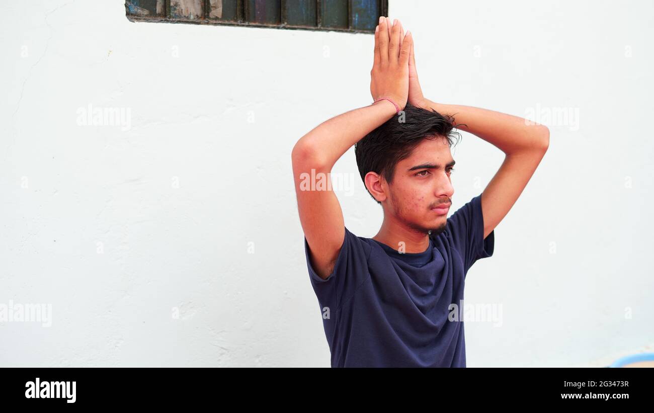 A boy is meditating at home in India. Indian young boy in a black traditional shirt sitting in a prayer position. Stock Photo