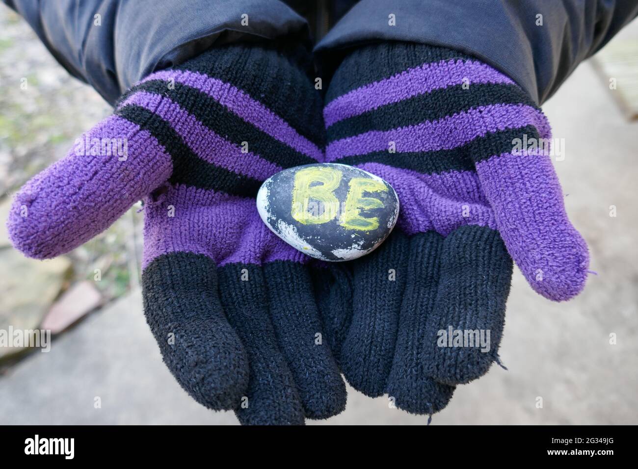 Person wearing black and purple gloves holding up kindness rock with BE message Stock Photo