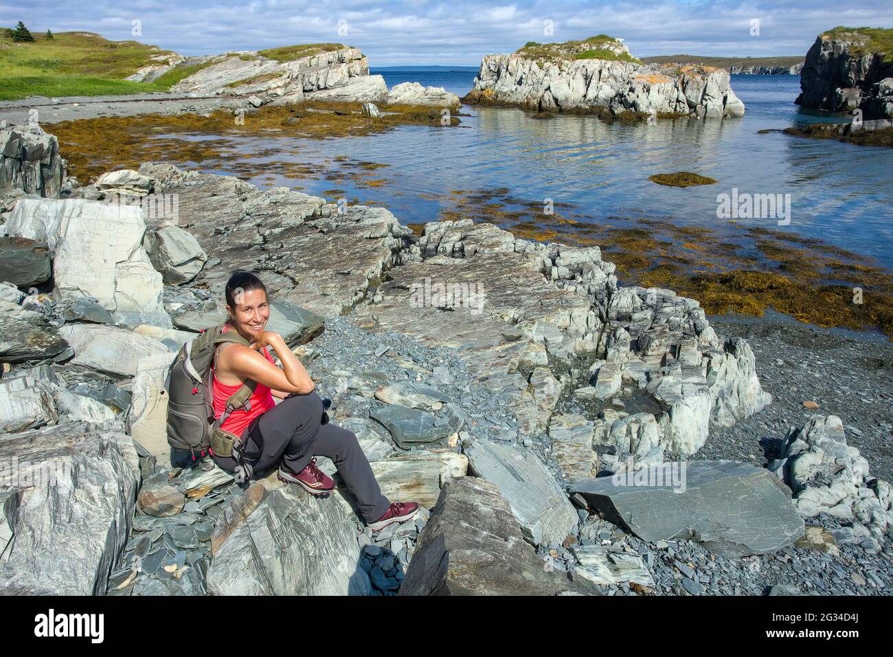 A fit female hiker wearing a backpack on the rocky Newfoundland coast near Bay Roberts. Stock Photo