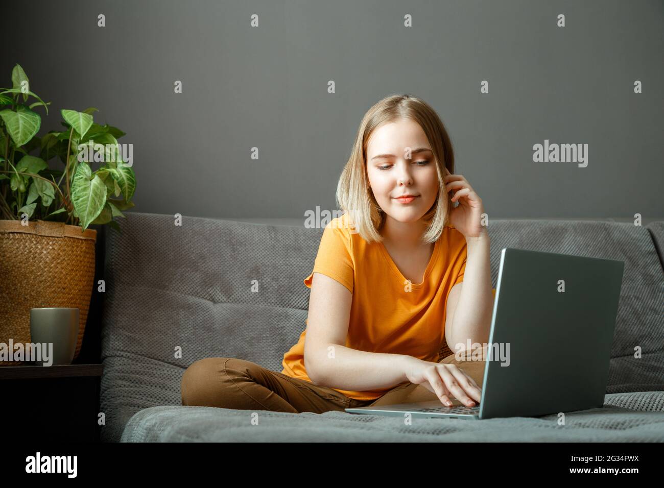 Pensive Caucasian beautiful woman work using laptop remotely from home. Portrait of teenage girl student thinking at home in living room studying Stock Photo